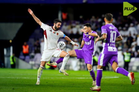 شعار نادي العين ونادي الوحدة مع كرة قدم في خلفية ملعب كرة قدم، يرمز إلى كلاسيكو الإمارات.