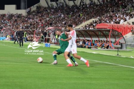شعار قناة رؤيا بجانب شعار الاتحاد الأردني لكرة القدم مع خلفية ملعب كرة قدم.